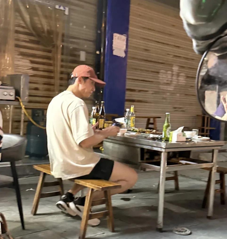 黄景瑜在乐山市一家路边摊吃烧烤，穿衣打扮很帅气，桌上放着好几瓶啤酒，路上人来人往