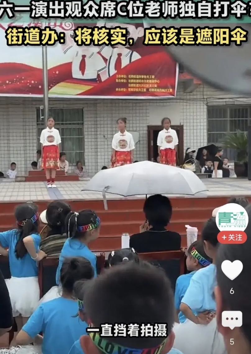贵州黔西某街道办六一儿童节演出现场，坐在C位的老师撑着伞看比赛，后面的人多次提醒