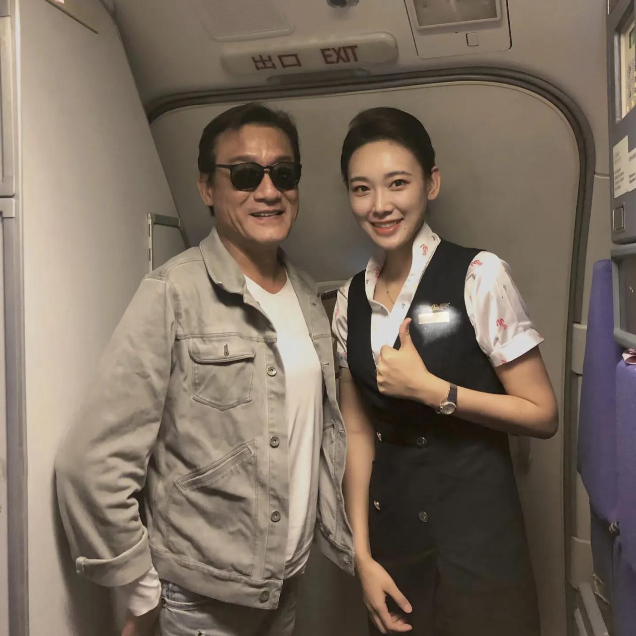 67岁梁家辉在飞机上和空姐合影，他的脸看起来很奇怪，下巴又长又歪，整张脸的五官很