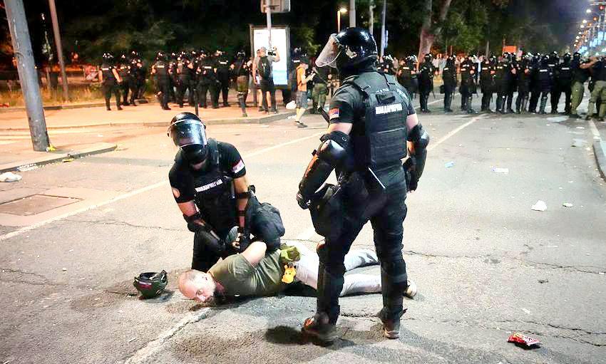 塞尔维亚防暴警察擒拿住一名骚乱者，此人腰间挂着一个黄色玩偶，五大三粗的汉子喜欢这