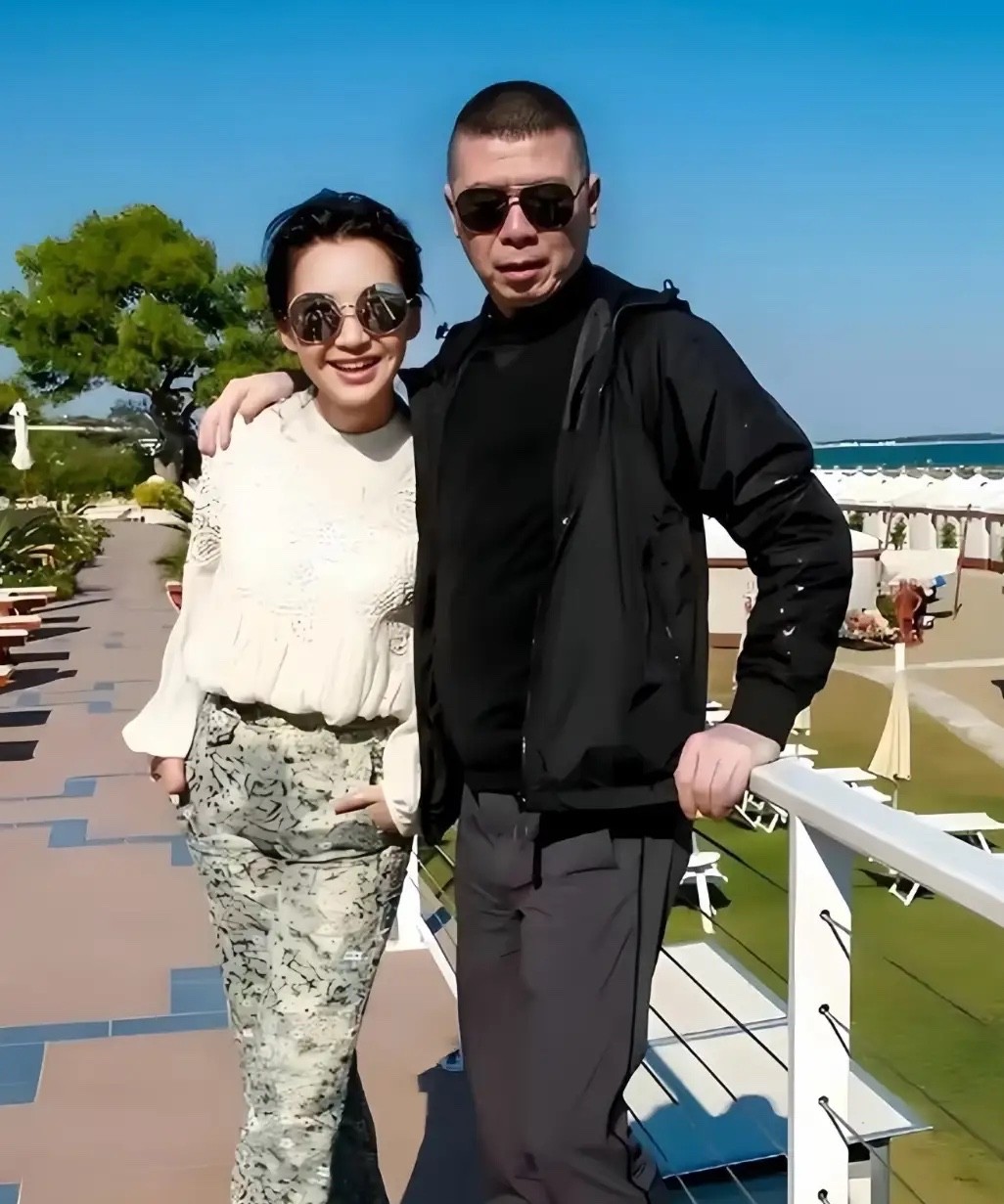 冯导演还挺有霸道总裁风范的，戴个墨镜，表情严肃，一手扶着栏杆，一手搭在美女肩膀上