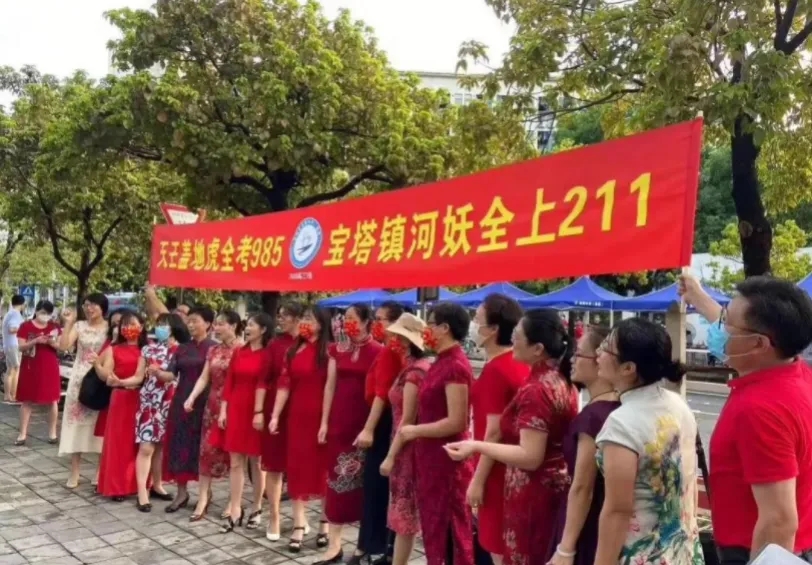 高考家长们穿旗袍寓意“旗开得胜”，举向日葵寓意“一举夺魁”，拿甘蔗上面挂上香蕉这