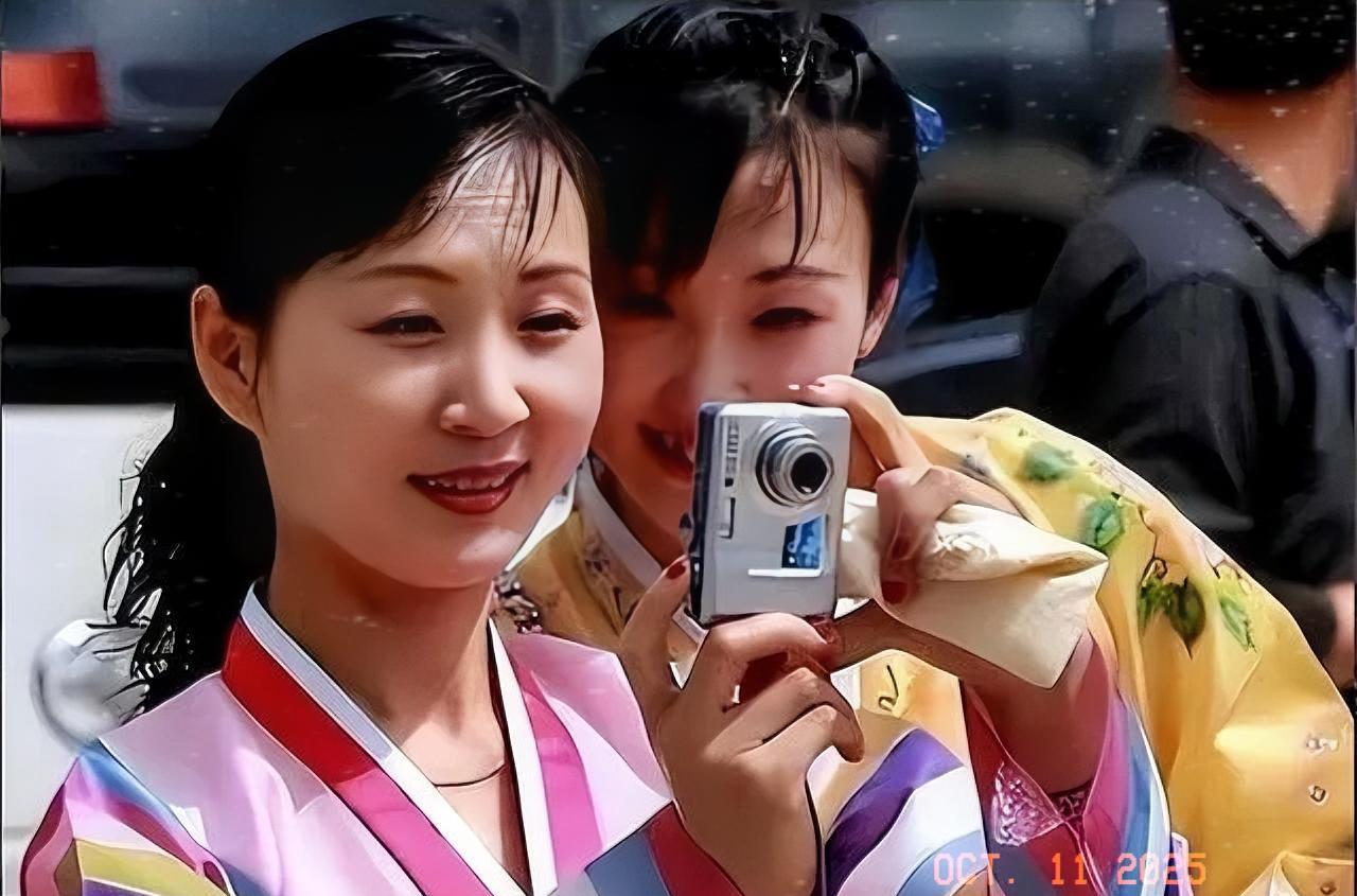 朝鲜两名女青年身着民族服装，正在用数码相机拍摄照片。