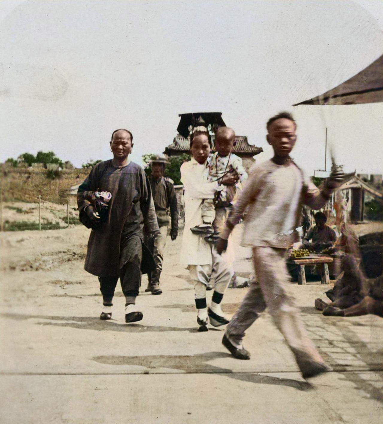 1912年，北京一个露天市场上，满族女子怀抱孩子逛街，身边跟着的是婆婆。当摄影师