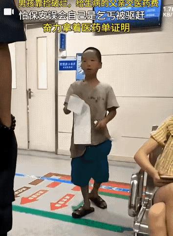 2021年，一个衣衫褴褛的小男孩一边拿着父亲的医药费账单，一边不停的向保安解释情