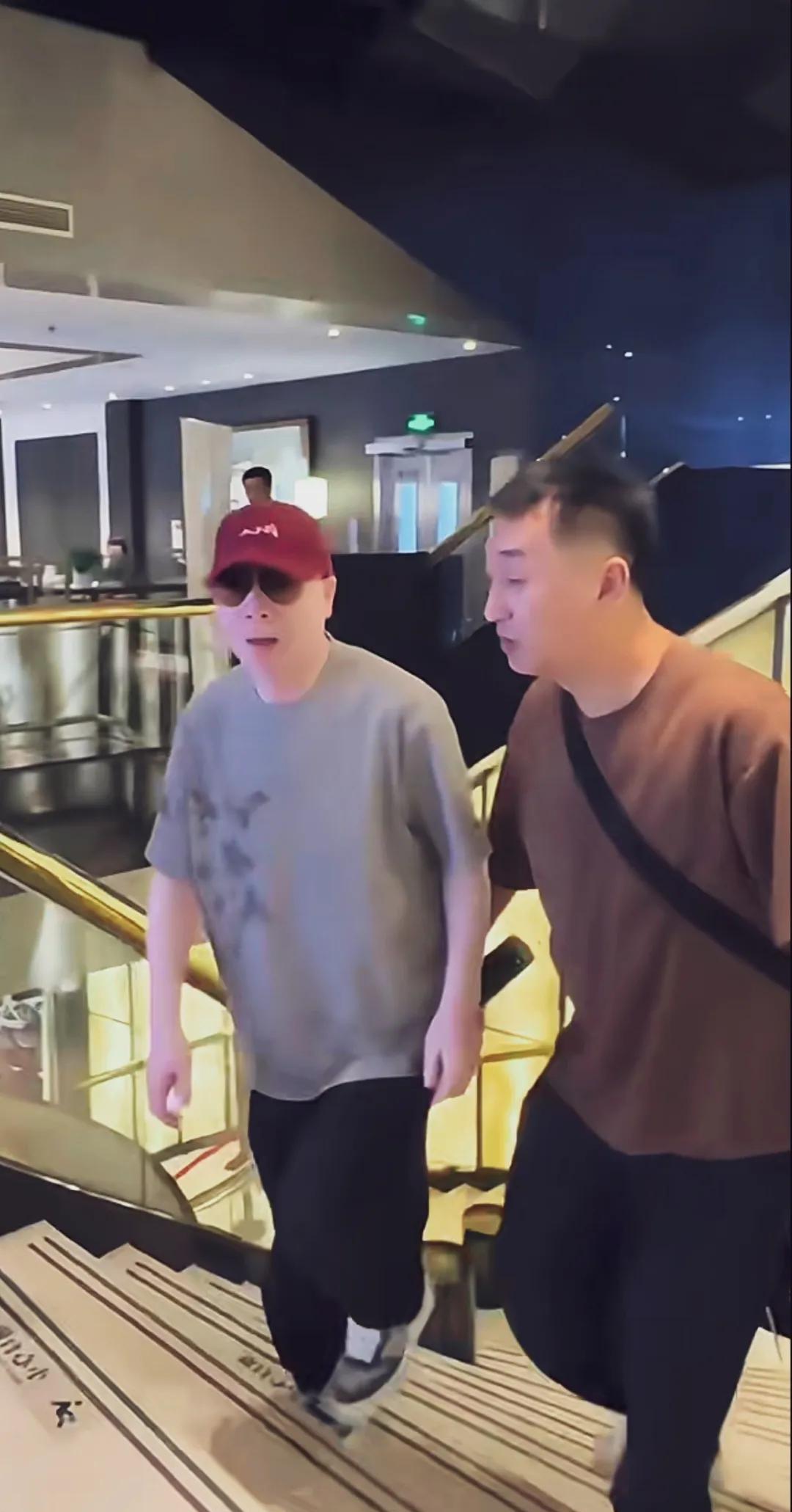大导演冯小刚身穿灰色体恤，头戴小红帽，精神健硕，皮肤雪白，生活中不苟言笑，很严肃