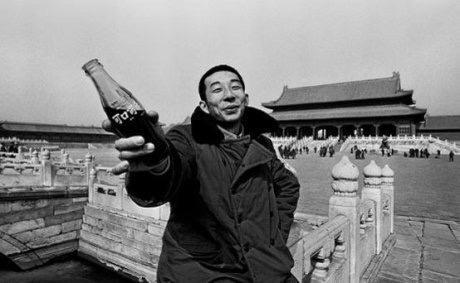1981年，一个穿军大衣的年轻人在北京故宫里举起一瓶可口可乐。 