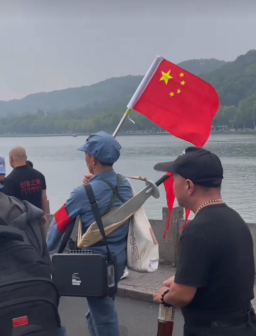 在杭州西湖断桥，有位身着红军衣服的大爷超吸睛。他腰挎手枪，身背大刀，手举国旗昂首