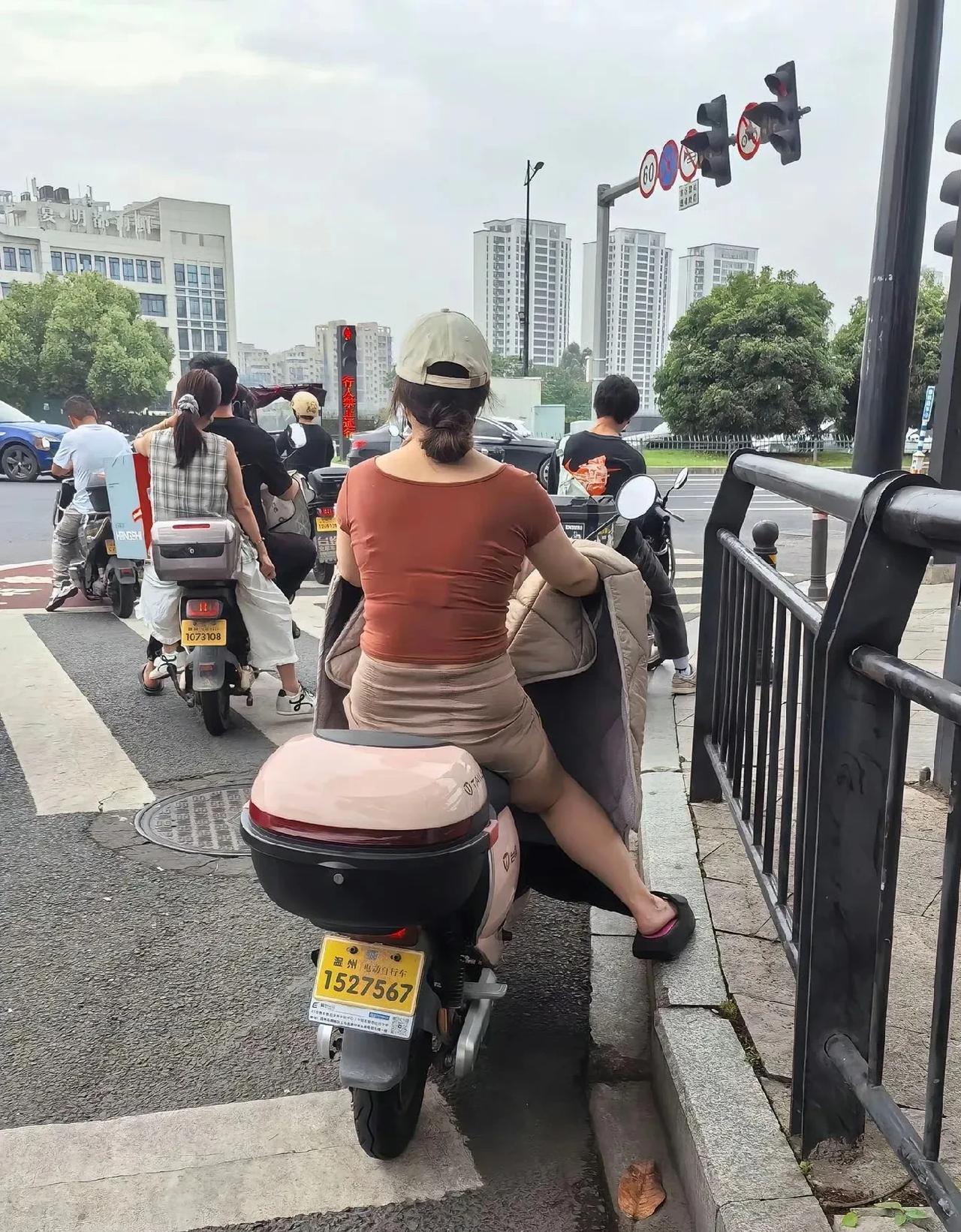 温州某地惊现这样一幕：
一群骑电动车的人在等红绿灯，
有的后座上还带着人，
可他
