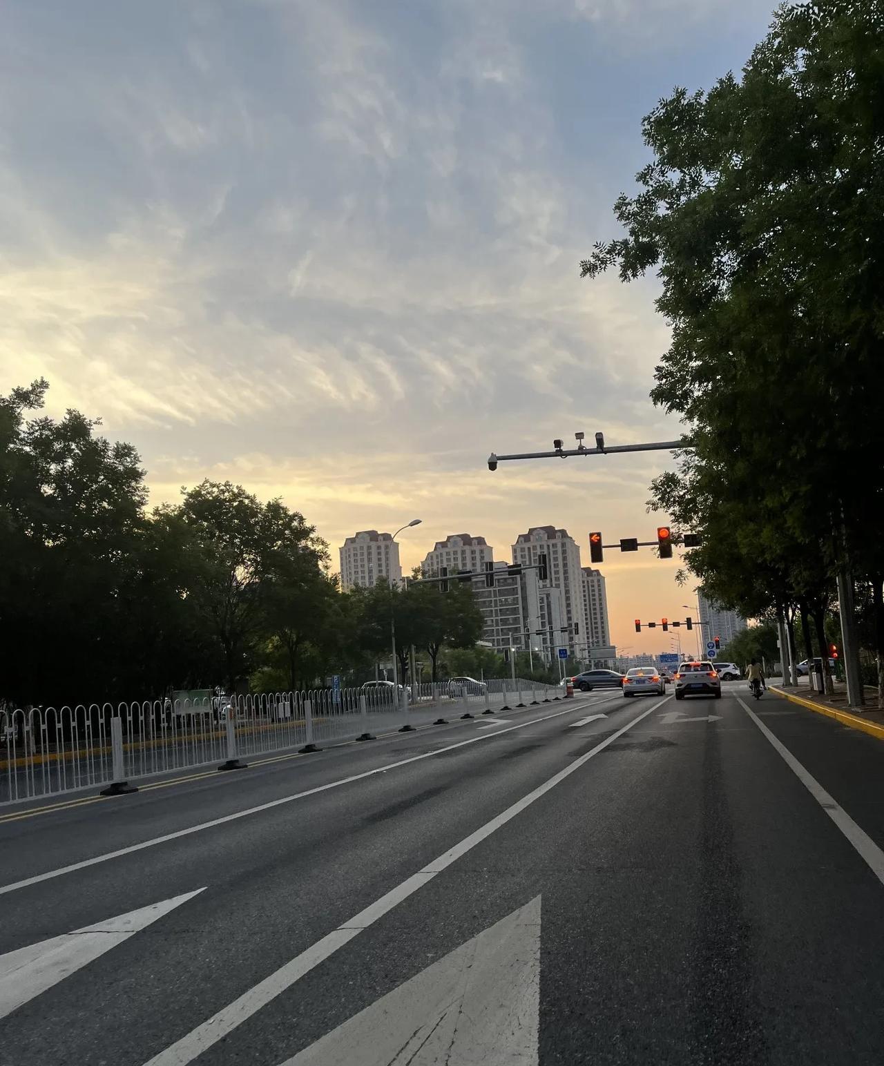 #谁有手机拍摄的夕阳原图发出来#暮色浸染城市道路，流云在天际漫卷，夕阳给高楼与绿