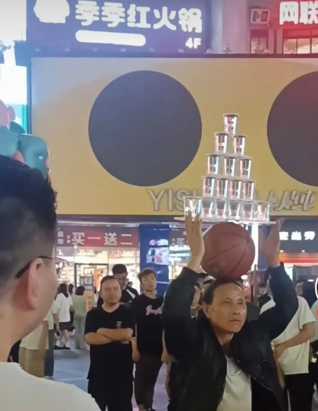 在长沙的步行街，有一名男子在街头表演杂技，男子先把一个篮球顶在头上，然后把倒满水