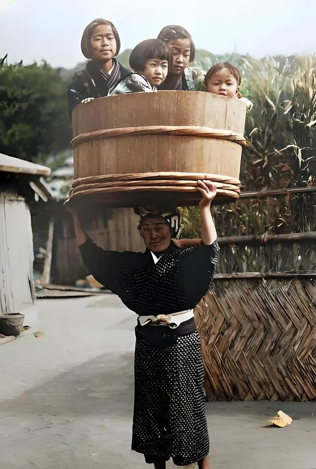 危险动作，请勿模仿。1900年，日本。一名妇女头上顶着一个硕大的木桶桶，里面装着