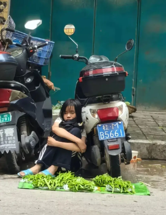 近日，广西一小女孩在路边摆卖青菜的视频在网上火热起来，小女孩依靠在一辆电动车睡着