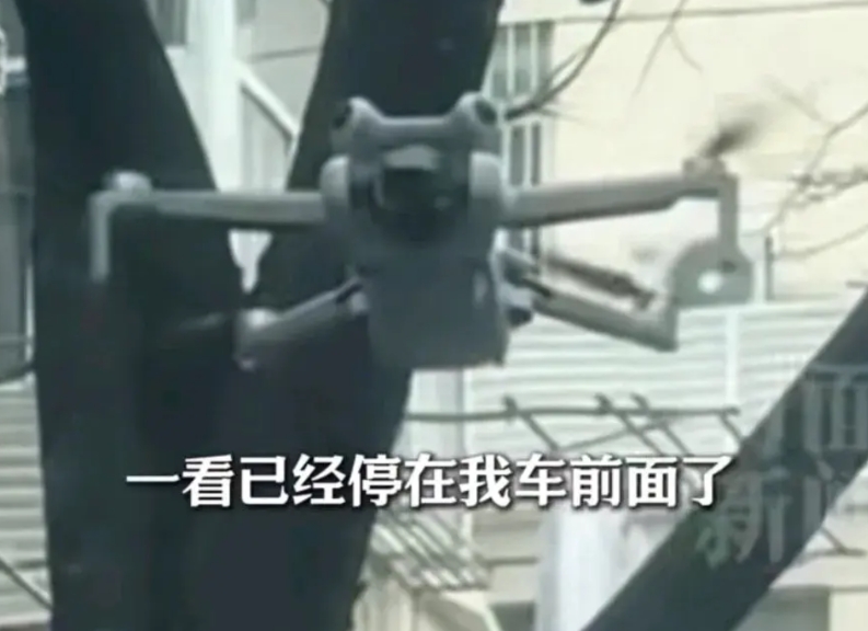 男子在路边违章停车，看见一架无人机停留在汽车斜前方，男子好奇的举起手机与无人机对