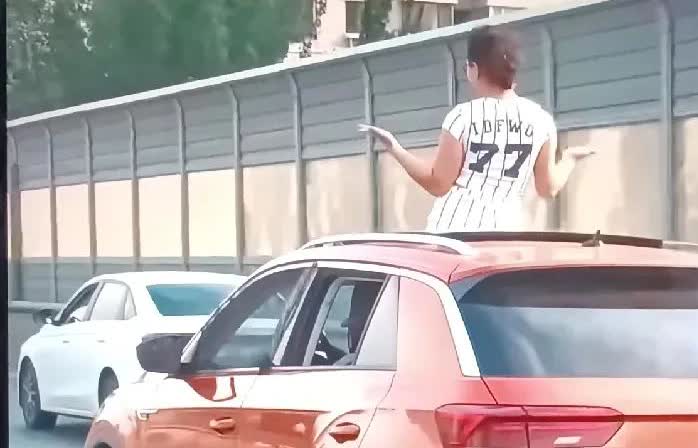 看到一条视频，在一条马路上，一辆红色小车正常行驶，后座上一个女子站起来，从天窗透