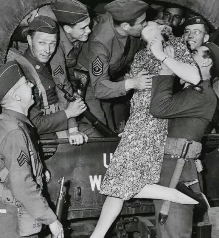 1940年代，一名士兵举起一名年轻的女人，将她送给卡车上的大兵。这名大兵不但亲吻