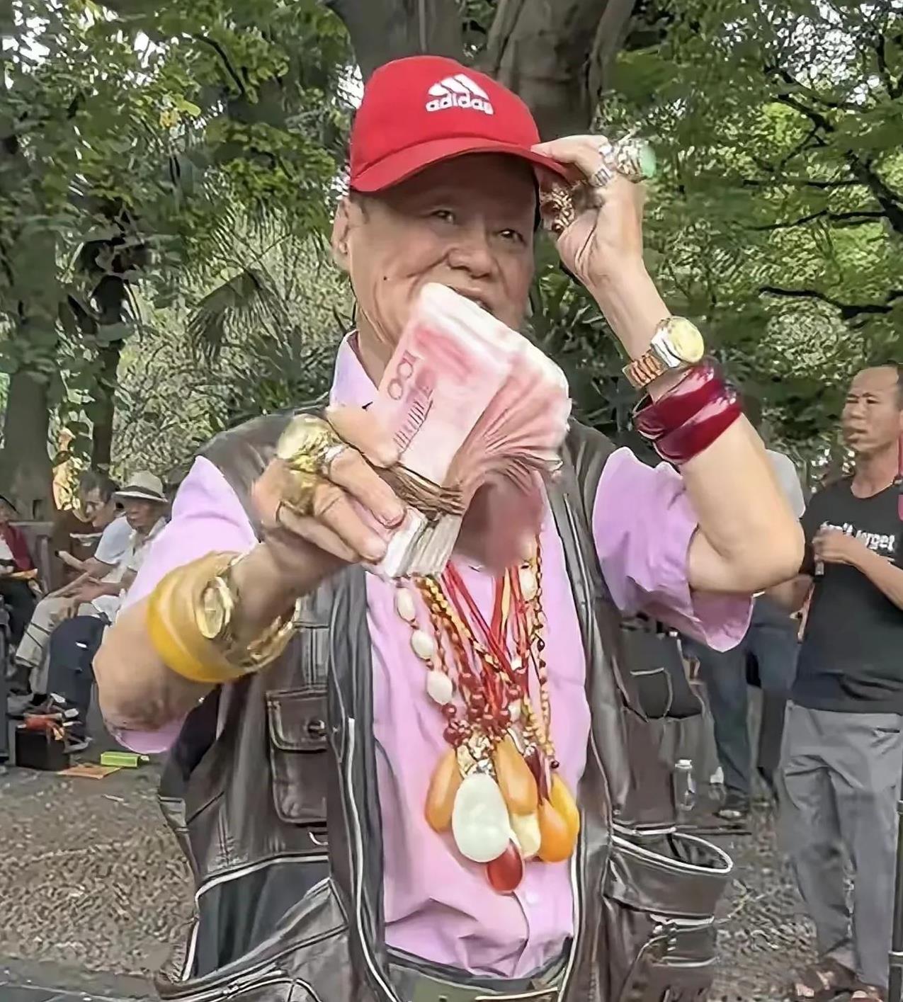 柳州鱼峰山下的这位大爷可真不简单，手持现金，浑身挂满珠宝想吸引合适的舞伴。然而，