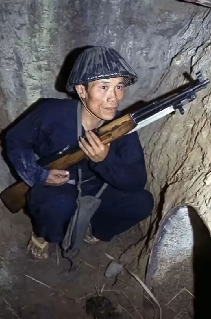 这是当年越南的一名民兵，他手握着中国支援的步枪，蹲在猫耳洞里，前面是一个大铁桶做