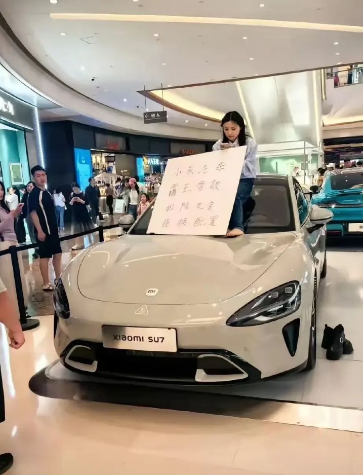 女人是善变的，小米汽车也表示无奈！

一女生爬上商场小米汽车上耍无赖，身边立牌上