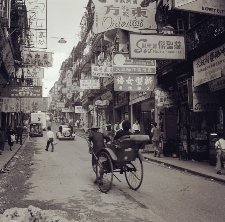  1955年的香港，狭窄的马路上，拉着人力车的车夫，街头到处可以看到广告牌。 