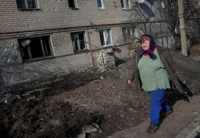 2022 年 2 月 22 日，一名乌克兰居民走在她被毁坏的房屋旁。