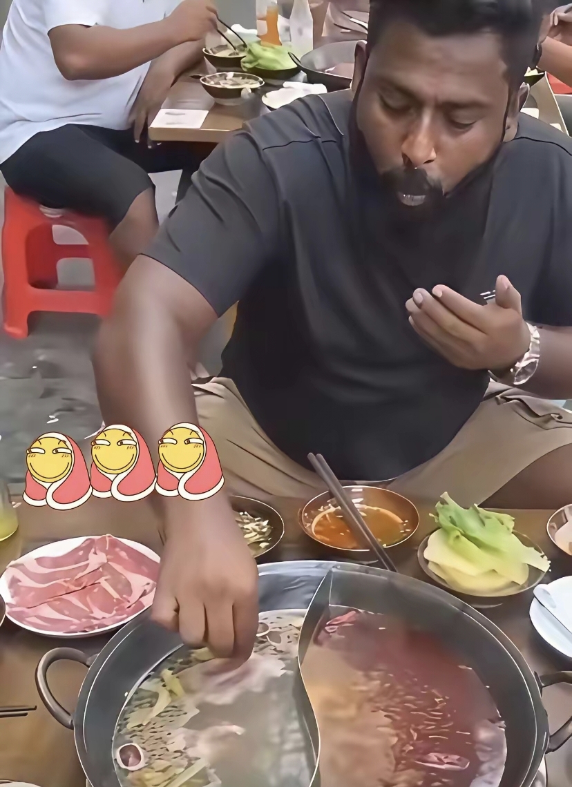 一位印度人在重庆火锅店用餐，满脸胡子拉碴，他放弃面前的筷子不用，张着大嘴，把手伸