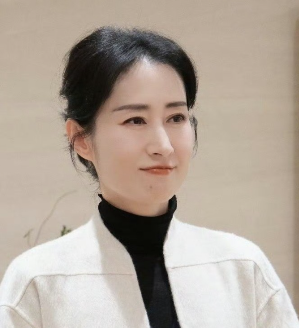 她穿着黑色长款大衣内搭米白围巾和深色高领
在天安门城楼前比出“耶”的手势，笑容松