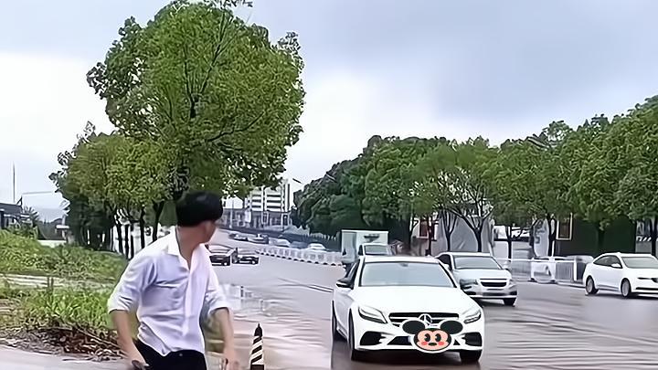 一男子见身后有车驶来，担心两名女子被雨水溅到，冲过去护住她们