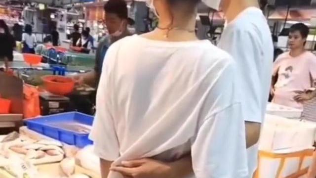 一女子在超市看阿姨剁鱼，之后紧紧抱着男朋友，男友搂着她的腰
