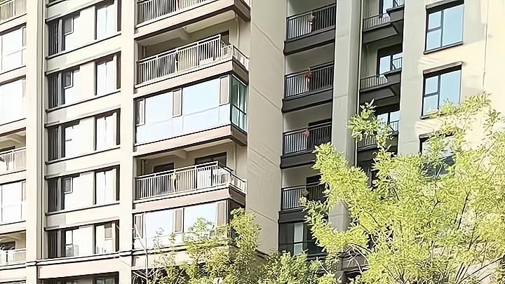 男子和一女子坐在草地上聊天，看到妻子路过，拿衣服挡住自己的脸