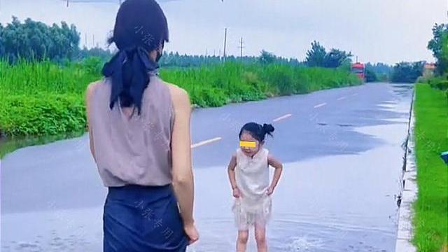 马路边，一女子脱掉高跟鞋，和女儿一起光脚踩水坑
