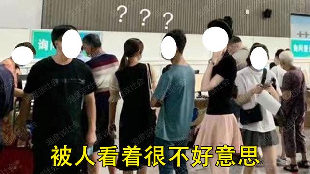 一女子排队用手压着裙子，裙子不是很长，脚还交叉夹在一起