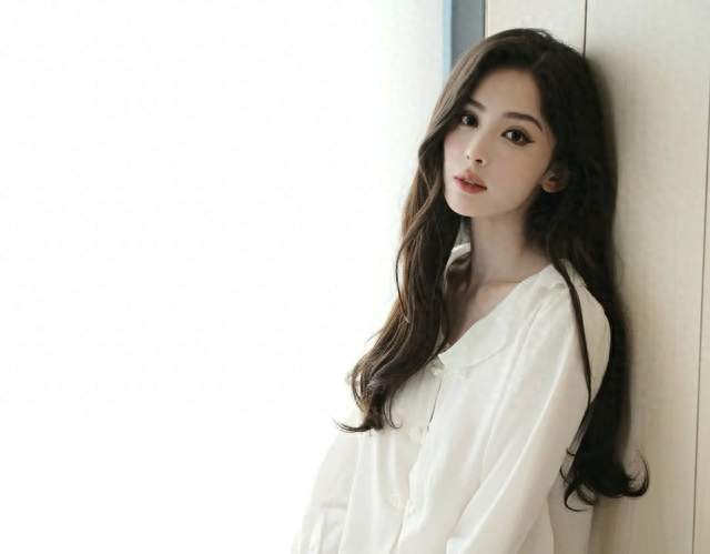 古力娜扎穿着白色居家服，光着脚坐在地板上，卷发披肩，慵懒随意