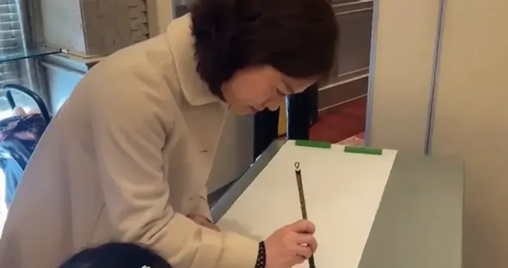 翁帆在香港参加春茗，她穿白色大衣很美，她写完毛笔字害羞的笑了