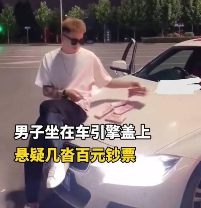 汪水芬说 河南一男子坐在汽车引擎盖上，拿起一张100元现金点燃，并拍视频