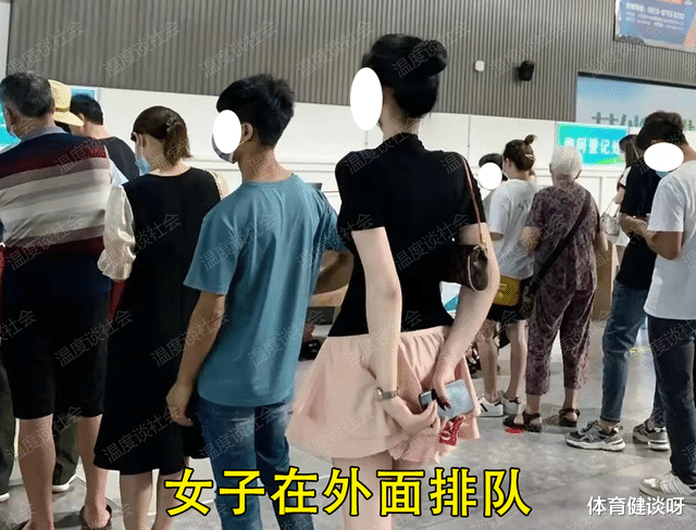 一女子排队用手压着裙子,裙子不是很长,脚还交叉夹在一起