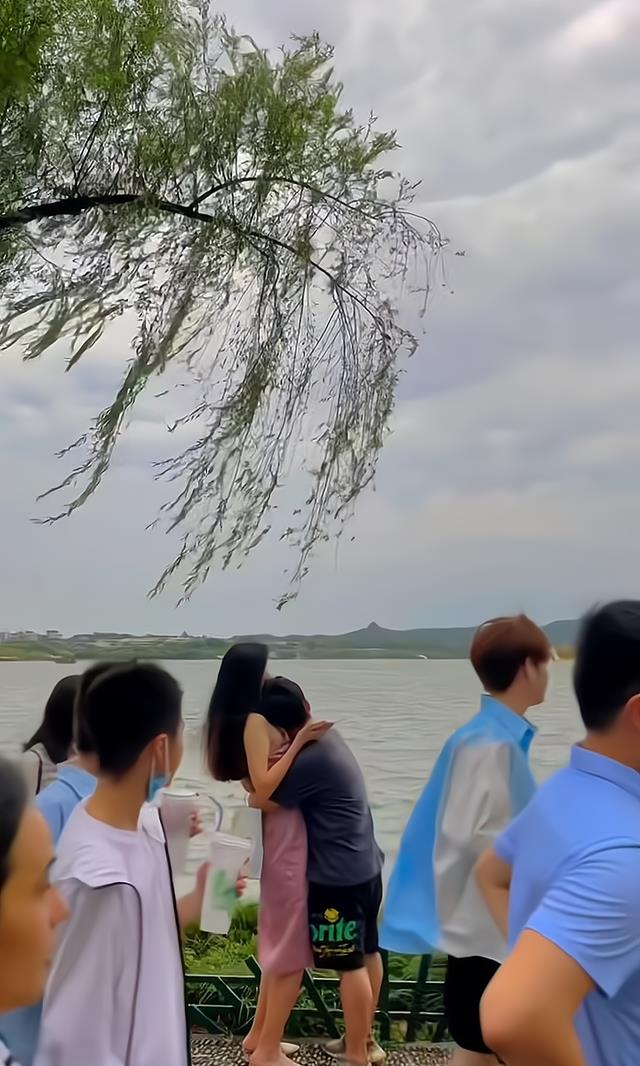 一男子在湖边,无视过往路人,和身高比自己高出半个头的女子相拥