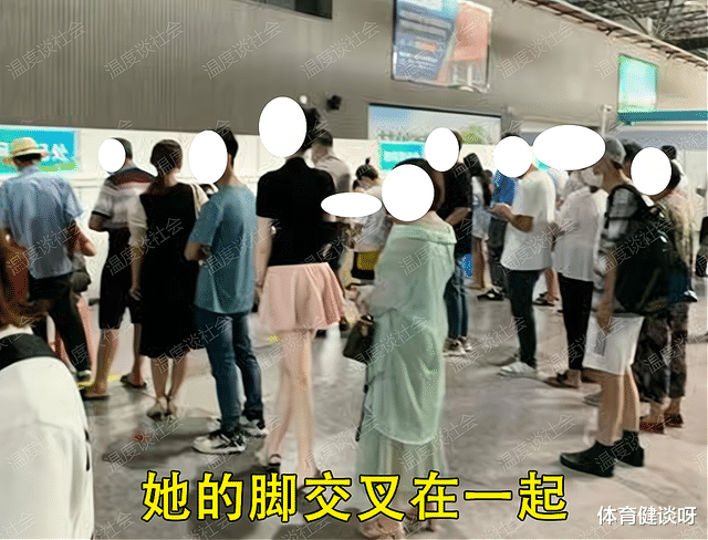 一女子排队用手压着裙子,裙子不是很长,脚还交叉夹在一起