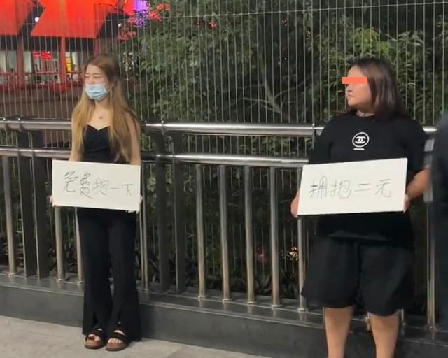 广东两女子夜晚站天桥边,举牌售卖拥抱,网友:收费的不一定好