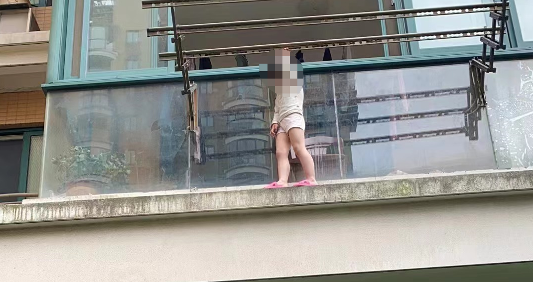 小女孩站在自家阳台外,双手紧紧握住阳台的晾衣架……