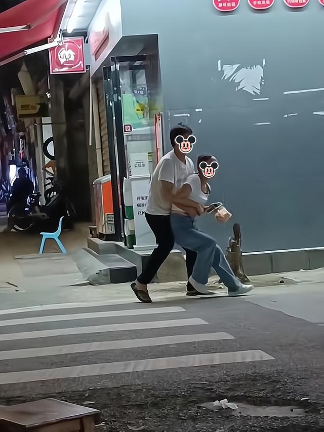 一男子担心喝醉酒的女友摔倒，抱着她走路，她却很不情愿