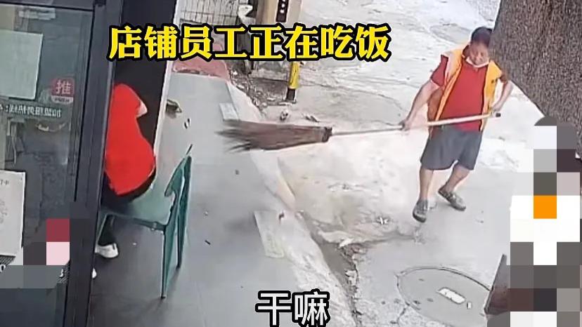 广东东莞，某店铺门口，一个红衣女子正在吃饭，一个身着清洁工装的男子拿着一把大扫帚