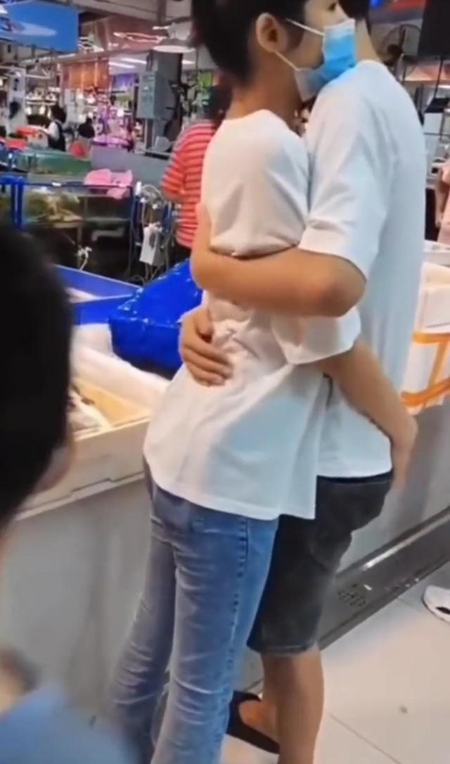 一女子在超市看阿姨剁鱼,之后紧紧抱着男朋友,男友搂着她的腰