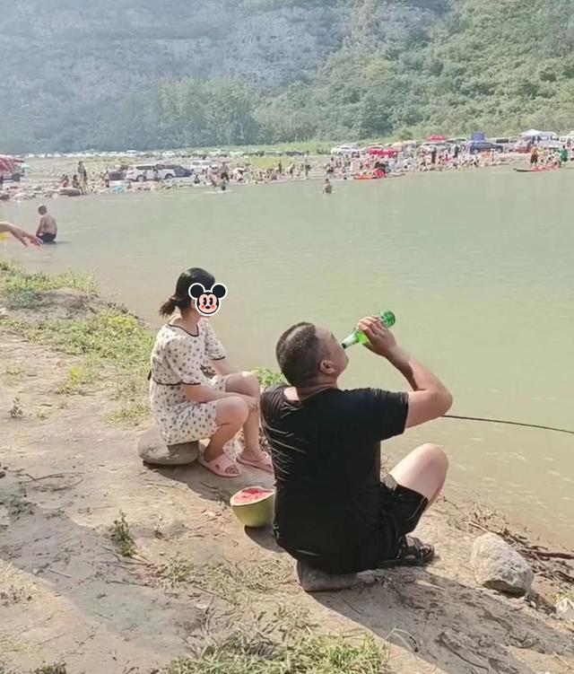 男子手持一瓶酒，坐在湖边和钓鱼的女子聊天，被老婆一脚踹到水里